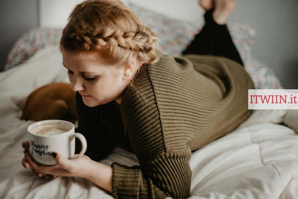 woman on bed holding white mug