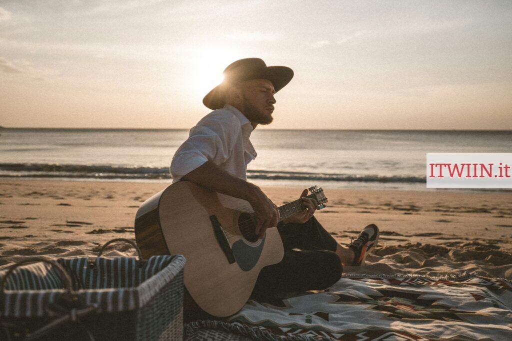 man in white dress shirt and brown cowboy hat playing acoustic guitar on beach during daytime
